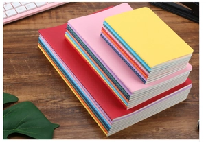 Multi-colored notebooks in A5 and B5 sizes stacked on a dark wood office desk
