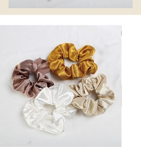 Dettaglio di quattro scrunchies in raso di seta nei toni marrone e oro lucido