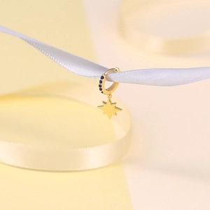 Detail of a gold star charm earring with blue sapphire stone on a silk ribbon