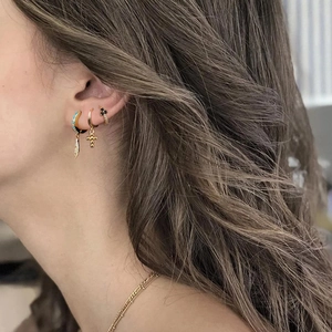 Detailed close-up of gold hoop earrings featuring turquoise feather and cross pendants