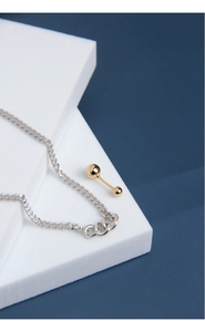 Close-up of minimalist S925 silver chain and polished golden ball pendant on geometry