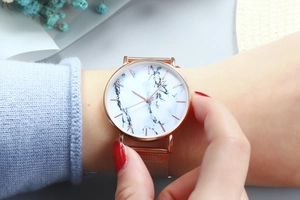Rose gold watch with white marble dial and mesh strap worn on a wrist in a lifestyle scene
