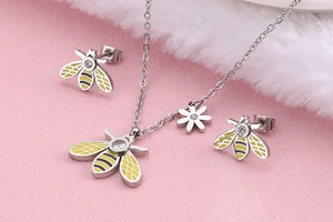 Detailed close-up of a silver bee jewelry set with crystals on a pink background