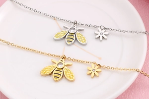 Detailed view of bee and flower charms on gold and silver titanium steel necklaces