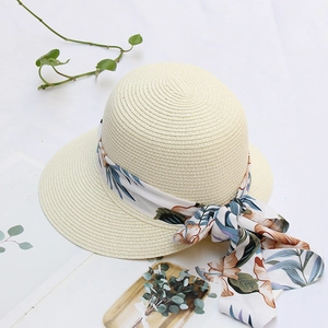Detail of beige straw sun hat with floral chiffon ribbon and bow on a white background