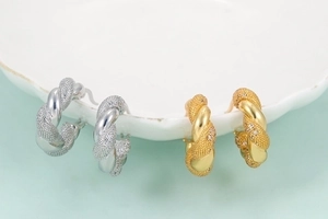Retro chunky twisted hoop earrings in gold and silver finish on a ceramic plate