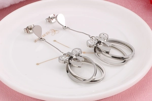 Close-up of silver bow drop earrings with double rings and white zircon in a ceramic dish