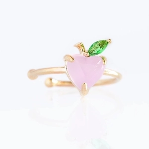 Detailed close-up of gold open ring with peach-shaped pink heart and green leaf gems