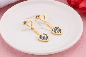 Détail de boucles d'oreilles cœur dorées avec strass sur assiette blanche et fleurs
