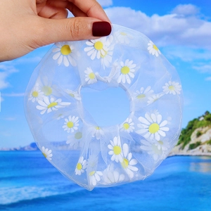 Daisy pattern organza hair scrunchie held against a sunny beach and ocean background