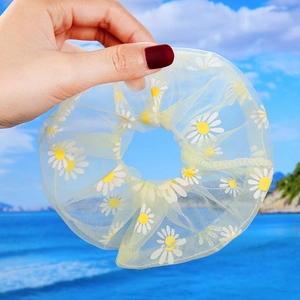 Detail of yellow daisy organza hair scrunchie held against a beach background