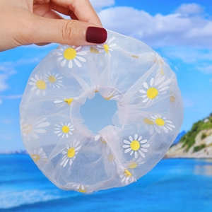 Detail of white organza scrunchie with yellow daisy print held against beach background