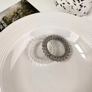 Detail of clear and dark grey spiral hair ties on a white ceramic plate decoration