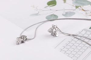 Detail of silver Hamsa hand and tree of life pendants on a sleek snake chain necklace