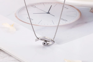 Macro shot of silver geometric eye pendant with fine snake chain on clock background