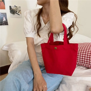 Detail of red canvas tote bag with gold snap closure shown in a lifestyle setting
