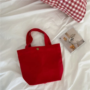 Detailed view of red canvas tote bag with metal clasp on a stylish white bed setting