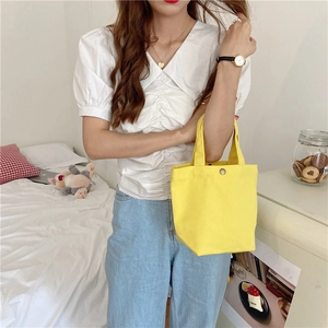 Detail of a bright yellow canvas tote bag with a metal snap button closure for daily use
