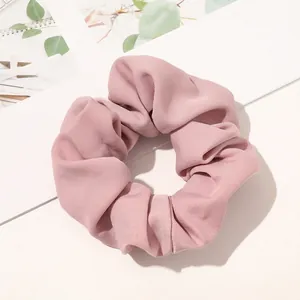 Detailed texture of pink plaid fabric scrunchie on a clean white desk with green plants