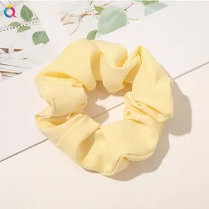 Close-up of a pale yellow fabric hair scrunchie with soft pleats on a white background