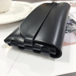 Close-up of minimalist black leather glasses case with flap closure on a white desk