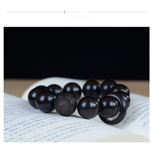 Détail d'un bracelet de perles en bois de santal foncé avec une perle centrale sculptée