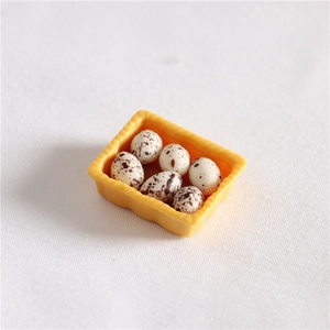 Macro view of a miniature dollhouse egg set featuring six resin eggs in a yellow tray