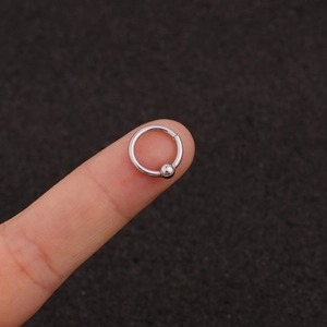 Macro shot of silver stainless steel piercing ring with bead on fingertip for size