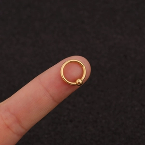 Macro shot of a small gold stainless steel captive bead ring held on a fingertip