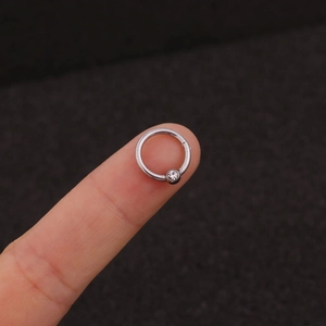 Detailed macro view of a silver stainless steel nose ring with a clear zircon stone on a finger