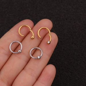 Stainless steel zircon septum rings in gold and silver finish on finger for ear piercing