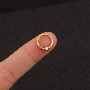 Golden hinged segment ring with sparkling zircon stone held on fingertip for size reference