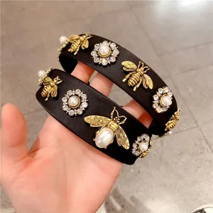 Baroque style wide black headbands with gold bees, pearls and rhinestones on grey tile
