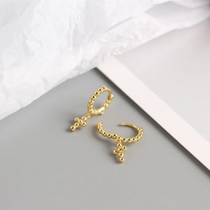 Detail of gold beaded hoop earrings featuring a hanging cross charm in polished metal