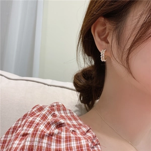 Close-up of elegant C-shaped earrings with woven white pearls and golden wire details