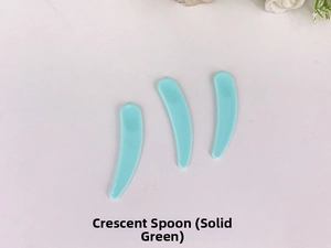 Three mint green plastic crescent scoops for cosmetics on a white surface with flowers