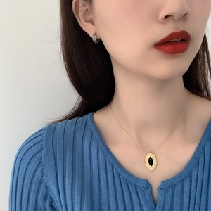 Detail of silver textured hoop earrings and black pendant necklace worn by a model