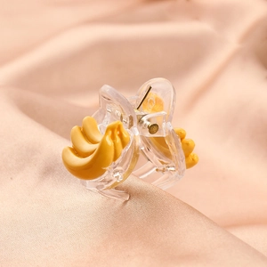 Close-up of cute banana acetate hair claw clip for kids on soft peach silk fabric