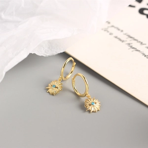 Detail of gold evil eye earring with turquoise bead on a stylish prop background