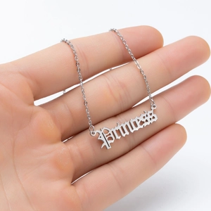 Gothic Princess lettering necklace in polished stainless steel held by hand for scale