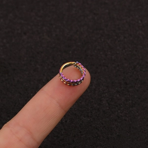 Close-up of rainbow metal twisted piercing ring held on fingertip for size reference