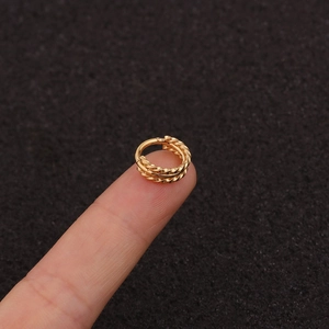 Macro shot of small golden braided hoop earring held on a finger with dark textured background