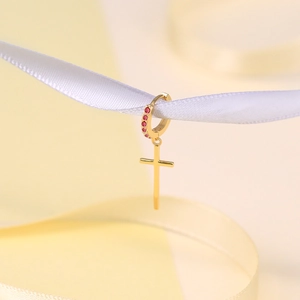 Detailed view of a gold S925 silver earring with a red stone cross pendant on a ribbon