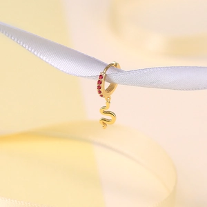 Macro shot of gold hoop earrings with snake pendant and red gemstones on white ribbon