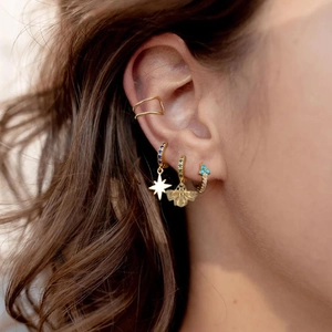 Detail of model wearing gold ear cuff and bee-shaped hoop earrings with green zircons