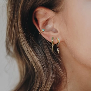 Detailed close-up of golden boho ear cuffs featuring green gems and feather pendants