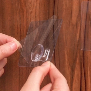 Transparent self-adhesive wall hooks shown being applied to a smooth wooden surface