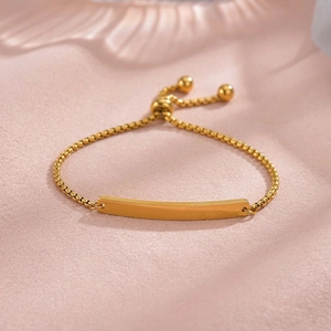 Close-up of adjustable gold box chain bracelet with smooth curved plaque and bead charm
