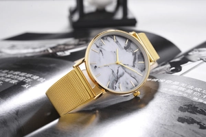 Detail shot of a minimalist gold mesh band watch with white marble pattern dial on a magazine