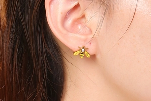 Close-up of golden bee stud earrings with yellow enamel and small diamond on model